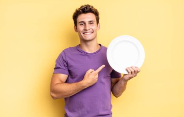 Neşeli bir şekilde gülümseyen, mutlu hisseden, kenarı ve yukarıyı gösteren, fotokopi uzayındaki nesneleri gösteren. boş tabak kavramı