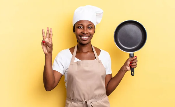 black afro chef woman smiling and looking friendly, showing number three or third with hand forward, counting down