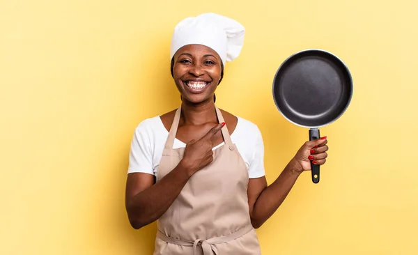 黒人アフロ料理人の女性は陽気に笑顔を浮かべ幸せを感じ横と上を指差しており — ストック写真