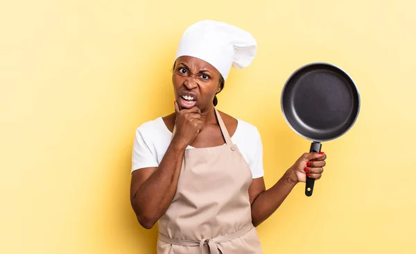 black afro chef woman with mouth and eyes wide open and hand on chin, feeling unpleasantly shocked, saying what or wow
