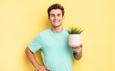 Mutlu bir şekilde gülümsüyor, eli kalçasında ve kendinden emin, olumlu, gururlu ve arkadaş canlısı bir tavırla. dekoratif bitki konsepti