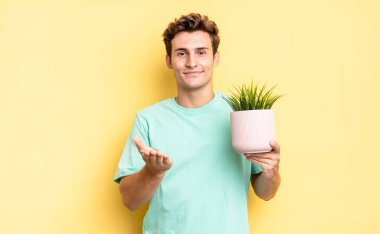 Mutlu bir şekilde gülümseyen, kendine güvenen, olumlu bakışlı, bir nesne ya da konsept sunan ve gösteren. dekoratif bitki konsepti