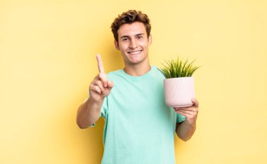 Gururla ve kendinden emin bir şekilde gülümseyerek bir numaralı pozu vererek, bir lider gibi hissederek. dekoratif bitki konsepti