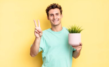 Gülümsüyor ve dost canlısı görünüyor. İki ya da iki numarayı gösteriyor. Elini ileri uzatıp geri sayıyor. dekoratif bitki konsepti