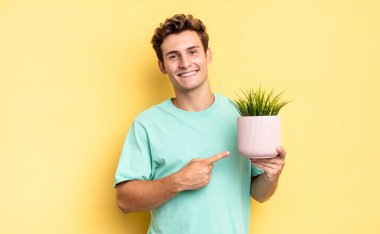 Neşeli bir şekilde gülümseyen, mutlu hisseden, kenarı ve yukarıyı gösteren, fotokopi uzayındaki nesneleri gösteren. dekoratif bitki konsepti