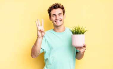 Gülümsüyor ve dost canlısı görünüyor. Üç ya da üç numarayı gösteriyor. Elleri önde, geriye doğru sayıyor. dekoratif bitki konsepti