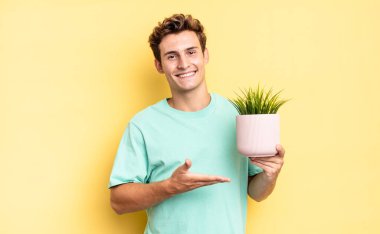 Neşeli bir şekilde gülümseyen, mutlu hisseden ve fotokopi uzayında avucunun içinde bir konsept gösteren. dekoratif bitki konsepti