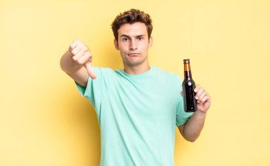 Kızgın, sinirli, hayal kırıklığına uğramış ya da hoşnutsuz, ciddi bir bakışla başparmaklarını aşağı gösteren. bira şişesi konsepti