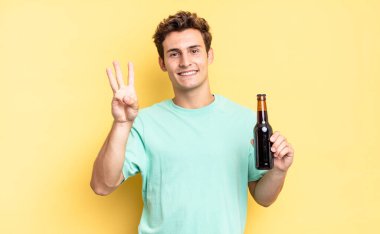 Gülümsüyor ve dost canlısı görünüyor. Üç ya da üç numarayı gösteriyor. Elleri önde, geriye doğru sayıyor. bira şişesi konsepti