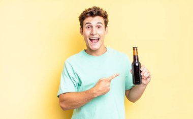 Heyecanlı ve şaşırmış görünüyor. Yana doğru ve yukarı doğru uzayı gösteriyor. bira şişesi konsepti