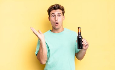 Şaşırmış ve şoke olmuş bir halde, çenesi düşmüş ve eli açık bir objeyi tutuyordu. bira şişesi konsepti