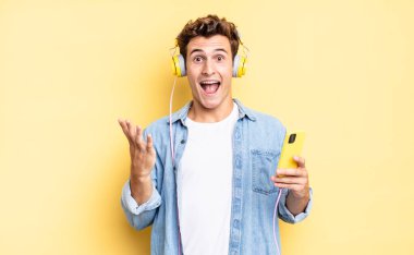 Mutlu, heyecanlı, şaşırmış ya da şok olmuş, gülümseyen ve inanılmaz bir şeye şaşırmış hissediyorum. kulaklıklar ve akıllı telefon konsepti