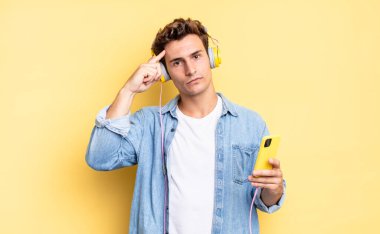 Kafan karışık ve şaşkın hissediyorsun. Deli, deli ya da aklını kaçırmış olduğunu gösteriyorsun. kulaklıklar ve akıllı telefon konsepti