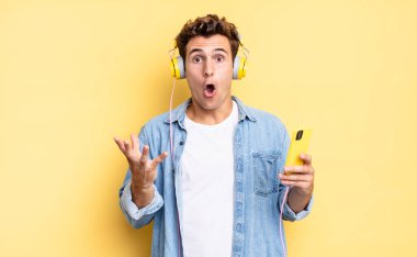 Açık sözlü ve şaşırmış, şok olmuş ve inanılmaz bir sürprizle şaşkına dönmüş. kulaklıklar ve akıllı telefon konsepti