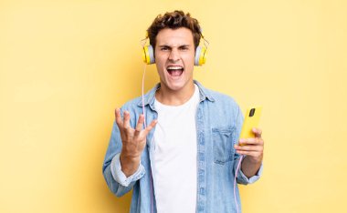 Kızgın, sinirli ve hayal kırıklığına uğramış görünüyorsun. Ne ya da neyin var diye bağırıyorsun. kulaklıklar ve akıllı telefon konsepti 