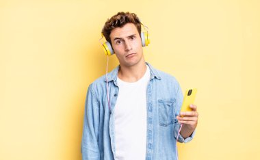 feeling puzzled and confused, with a dumb, stunned expression looking at something unexpected. headphones and smartphone concept