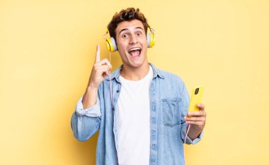 Bir fikri fark ettikten sonra mutlu ve heyecanlı bir dahi gibi hissetmek, neşeli bir şekilde parmak kaldırmak, eureka! kulaklıklar ve akıllı telefon konsepti