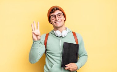 Gülümsüyor ve dost canlısı görünüyor. Üç ya da üç numarayı gösteriyor. Elleri önde, geriye doğru sayıyor. öğrenci konsepti