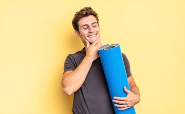 Mutlu, kendinden emin bir ifadeyle gülümsüyor, çenesinde elle, merakla yan tarafa bakıyor. yoga mat konsepti