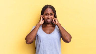 Afro siyah güzel kadın sinirli, stresli ve sinirli görünüyor, iki kulağını da sağır edici bir ses, ses ya da yüksek sesle kapatıyor