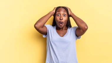 Afro siyah güzel bir kadın heyecanlı ve şaşırmış görünüyor, ağzı açık, iki eli başında, kendini şanslı bir kazanan gibi hissediyor.