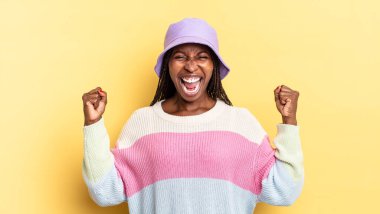 Afro siyah güzel kadın mutlu, şaşırmış ve gururlanmış hissediyor, bağırıyor ve başarıyı büyük bir gülümsemeyle kutluyor.