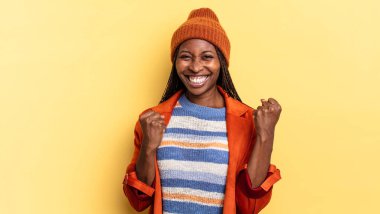 Afro siyah güzel kadın zaferle bağırıyor, gülüyor, mutlu ve heyecanlı hissediyor başarıyı kutlarken.