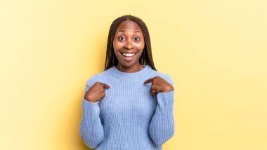Afro siyah güzel bir kadın mutlu, şaşırmış ve gururlanmış hissediyor, heyecanlı ve şaşkın bir bakışla kendini işaret ediyor.