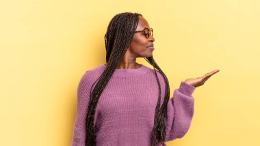 Afro siyah güzel bir kadın mutlu ve güler yüzlü, elinde tuttuğu bir nesneye ya da konsepte bakıyor.