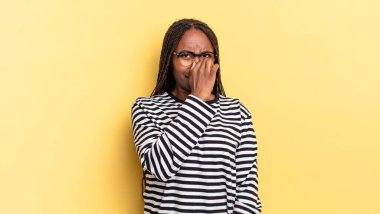 Afro siyah güzel kadın iğreniyor, kötü ve nahoş bir koku duymamak için burnunu tutuyor.