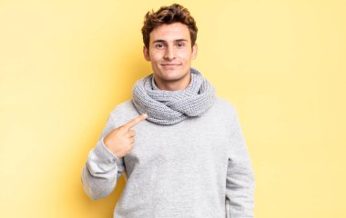 Genç çocuk gururlu, kendinden emin ve mutlu görünüyor, gülümsüyor ve kendini işaret ediyor ya da bir numaralı işareti yapıyor.