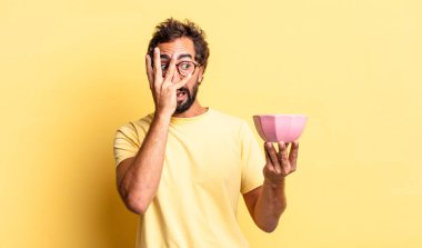 Şok olmuş, korkmuş ya da dehşete düşmüş gibi görünen, yüzü elle kaplanmış ve saksıyı tutan çılgın bir adam.