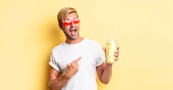 Blondynka Dorosły Mężczyzna Wygląda Podekscytowany Zaskoczony Wskazując Stronie Milkshake — Zdjęcie stockowe