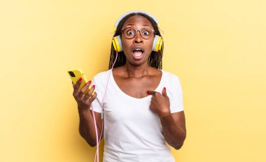 Şok olmuş ve şaşırmış bir halde, ağzı açık, kendini işaret eden ve müzik dinleyen