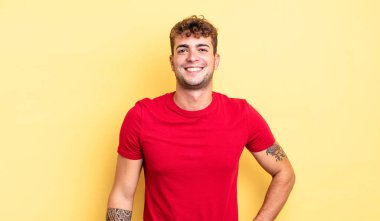 Genç yakışıklı adam kameraya çapraz kollarıyla gülümsüyor ve mutlu, kendinden emin, tatmin olmuş bir ifade, yan bakış.