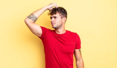 Genç yakışıklı adam şaşkın ve şaşkın hissediyor, başını kaşıyor ve yana bakıyor.