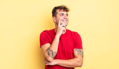 Genç yakışıklı adam mutlu bir şekilde gülümsüyor ve hayal kuruyor ya da şüphe ediyor.