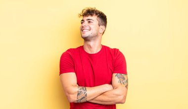 Genç yakışıklı adam mutlu, gururlu ve umutlu, merak ediyor ya da düşünüyor, çapraz kollarla boşluğu dolduruyor.