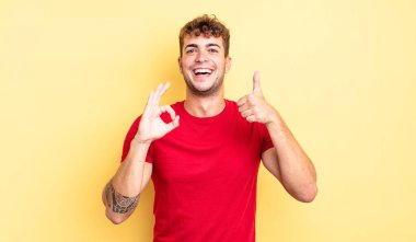 Genç yakışıklı adam kendini mutlu, şaşkın, tatmin olmuş ve şaşırmış hissediyor, tamam gösteriyor ve el kol hareketleri yapıyor, gülümsüyor.