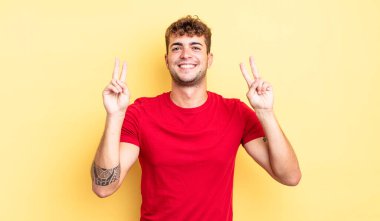 Genç yakışıklı adam gülümsüyor ve mutlu görünüyor, arkadaş canlısı ve memnun, işaret eden zafer ya da barış iki elle