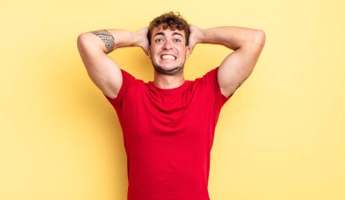 Genç ve yakışıklı bir adam stresli, endişeli, endişeli ya da korkmuş, elleri başının üstünde, hata yaptığında panikliyor.