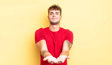 Genç yakışıklı adam mutlu bir şekilde gülümsüyor arkadaş canlısı, kendinden emin, olumlu bakışlı, bir nesne ya da konsept sunuyor ve gösteriyor.