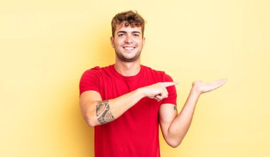 Genç yakışıklı adam gülümsüyor, mutlu, tasasız ve tatmin olmuş hissediyor, fotokopi alanındaki konsepte ya da fikre işaret ediyor.