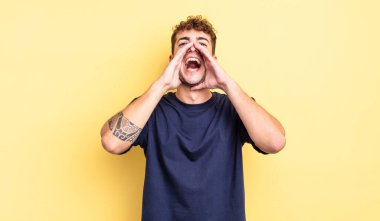 Genç yakışıklı adam mutlu, heyecanlı ve pozitif hissediyor. Elleri ağızda, bağırıyor.