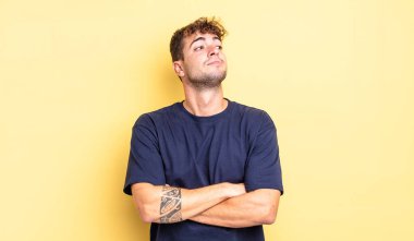 Genç yakışıklı adam omuz silkiyor, kafası karışık ve kararsız, kolları bağlı ve şaşkın görünüyor.