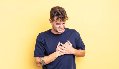 Genç yakışıklı adam üzgün, yaralı ve kalbi kırık görünüyor, iki elini de kalbine yakın tutuyor, ağlıyor ve bunalımda.