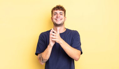 Genç yakışıklı adam kendini mutlu ve başarılı hissediyor, gülümsüyor ve alkışlıyor, alkışlarla tebrik ediyor.