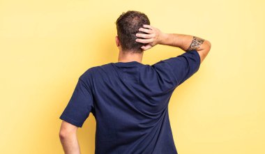 Genç yakışıklı adam düşünüyor ya da şüphe ediyor, kafasını kaşıyor, şaşkın ve kafası karışık hissediyor, arkaya ya da arkaya bakıyor.