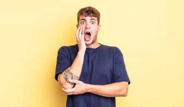 Genç yakışıklı adam şok ve inançsızlık içinde, elleri yanak ve kolları çapraz, sersemlemiş ve şaşırmış hissediyor.