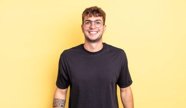 Genç yakışıklı adam mutlu ve şapşal görünüyor. Geniş, eğlenceli, kaçık bir gülüşü ve açık gözleri var.